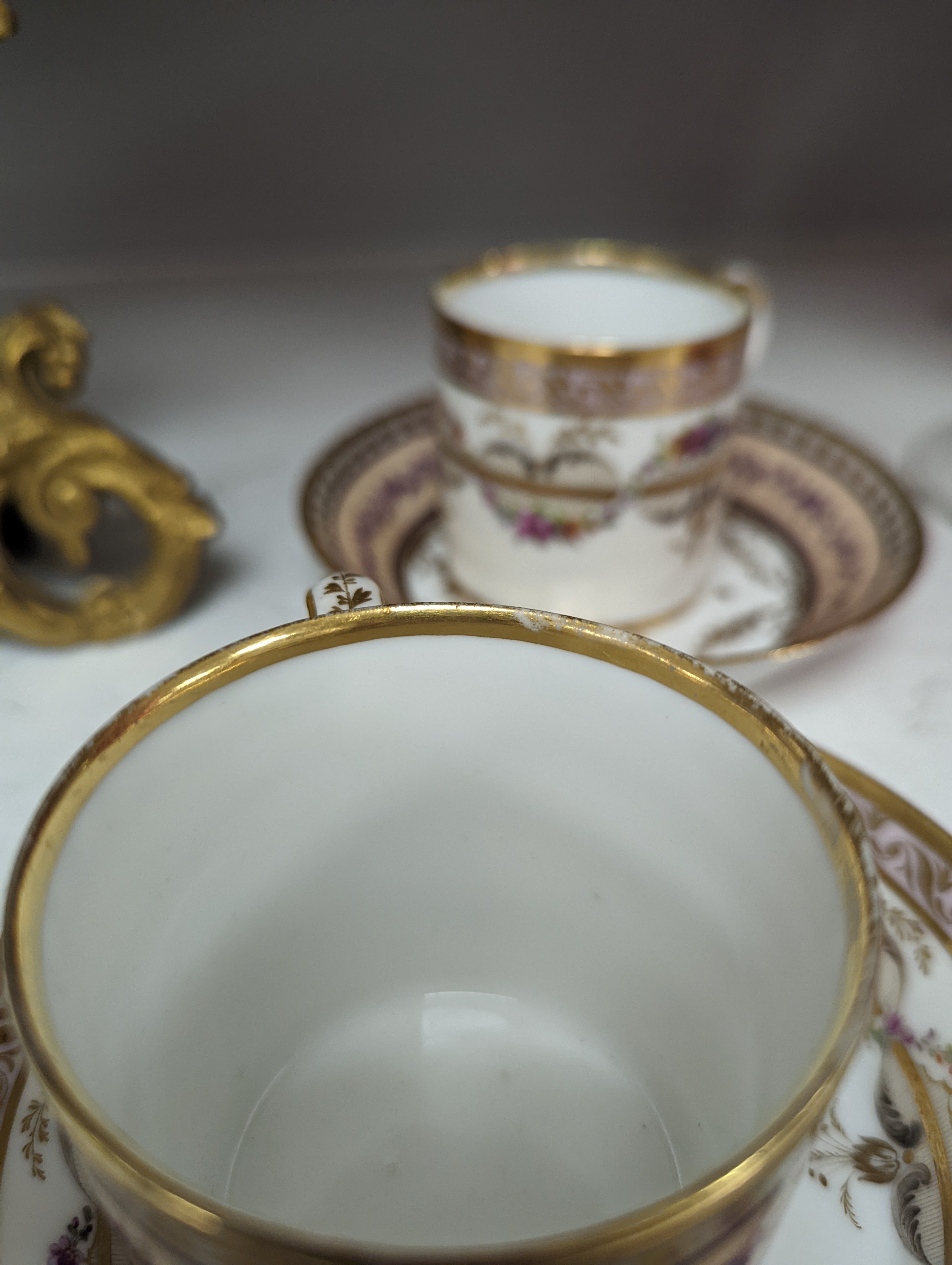 A Duc d'Angouleme coffee can and saucer painted with a puce chain of leaves on a salmon coloured ground and another painted with a flower chain, black feather and a gilt line, latter with stencilled red mark 'Manuf de M